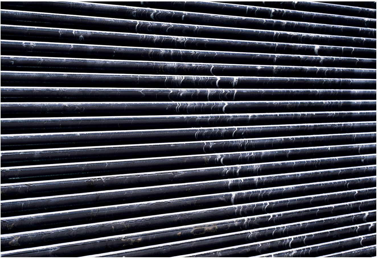 The image shows a close-up view of horizontal black metal pipes or rods with streaks of white residue, creating an abstract industrial texture.