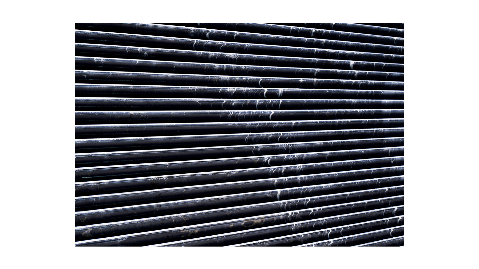 The image shows a close-up view of horizontal black metal pipes or rods with streaks of white residue, creating an abstract industrial texture.