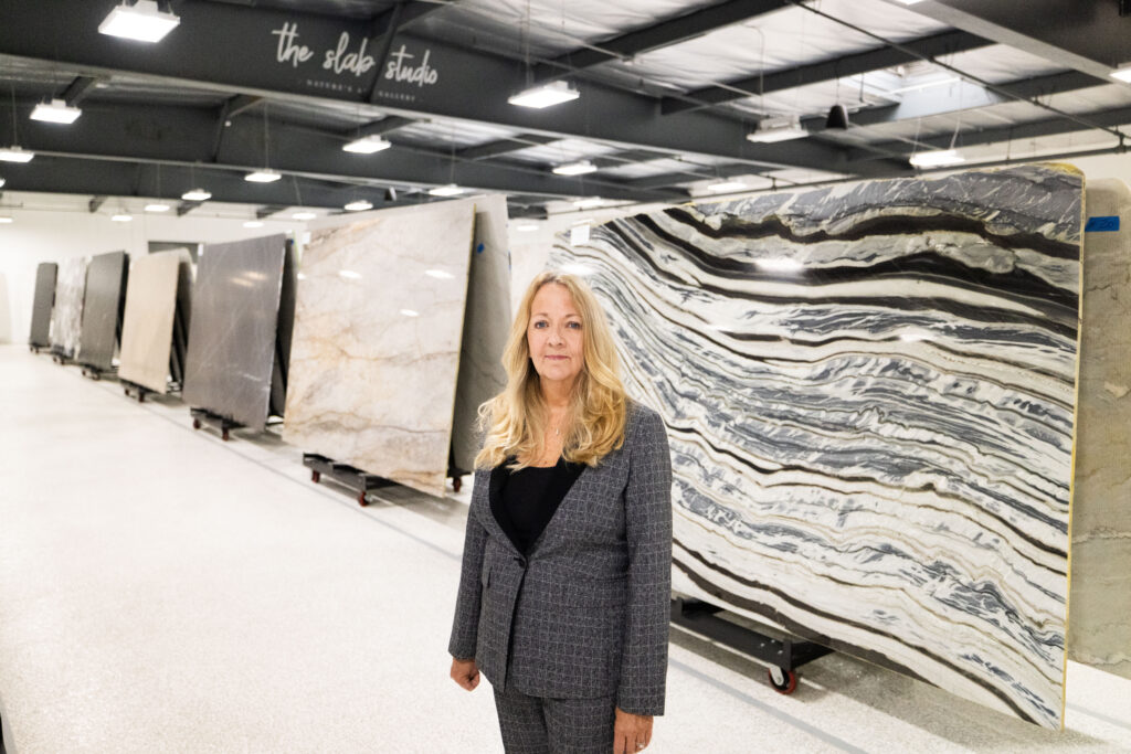 Jill Kummer standing in front of premium marble and quartzite slabs at The Slab Studio showroom in Santa Ana, California.