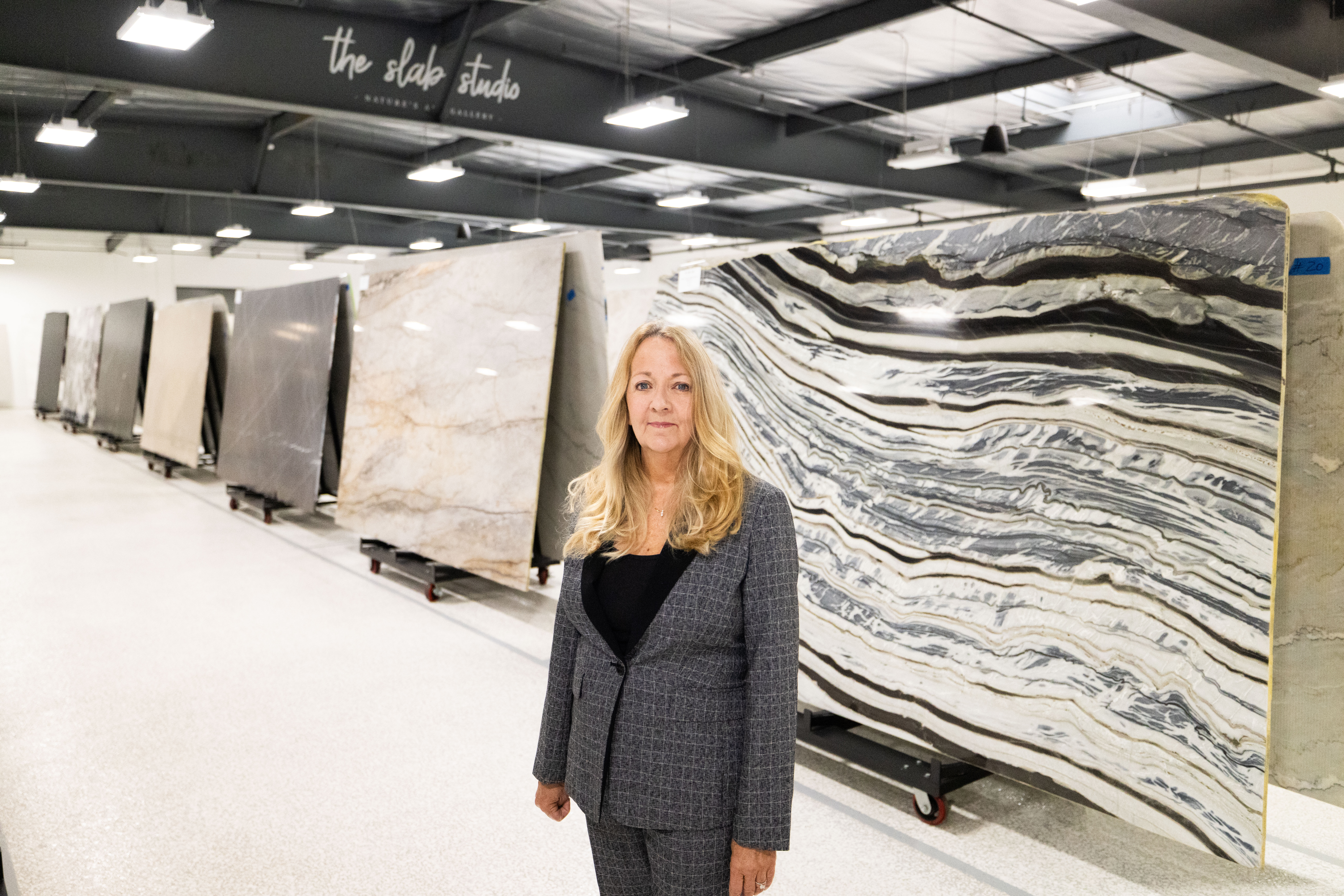 Jill Kummer standing in front of premium marble and quartzite slabs at The Slab Studio showroom in Santa Ana, California.
